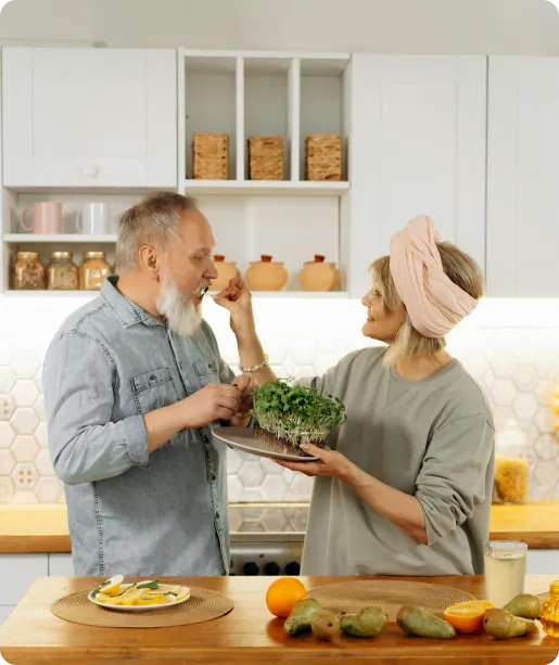 Elderly couple in kitchen sharing salad with smiles, symbolizing healthy aging through Eastern Medicine